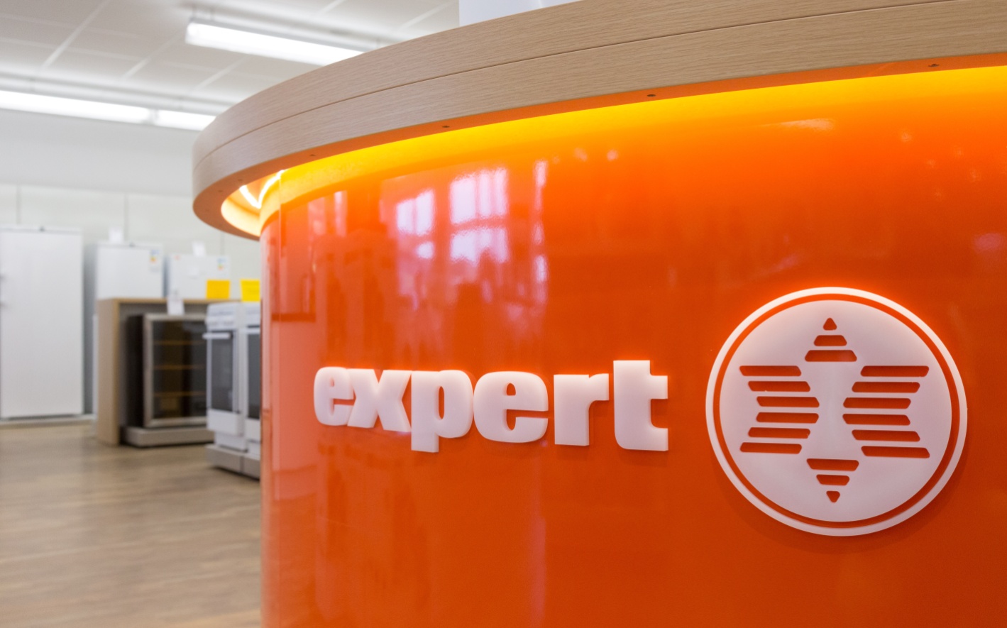 Nahaufnahme des weißen expert-Logos auf einem orangefarbenen Pult im Elektrogeschäft.