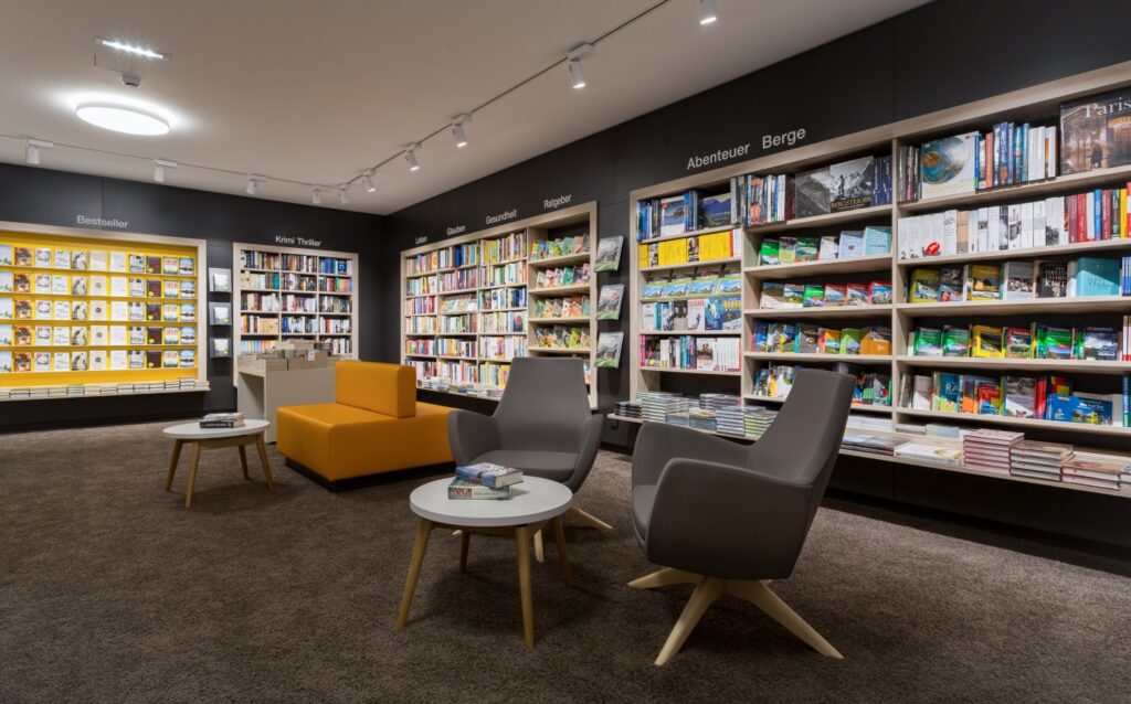 Verkaufsraum mit drei Lichtebenen – Grundlicht von der Decke, Zonenlicht über einer Leseecke und Akzentlicht auf der Bestseller-Wand