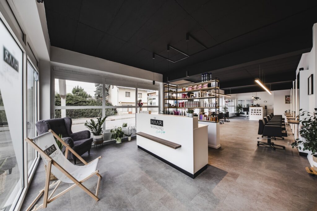 Großer Friseursalon mit großzügigem Empfangsbereich, Markenbranding, Lounge-Zone und Welonda-Ausstattung im hinteren Bereich