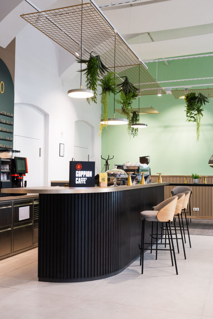 Modern cafe interior with a curved black counter and hanging planters above the seating area by bar stools on the right side.